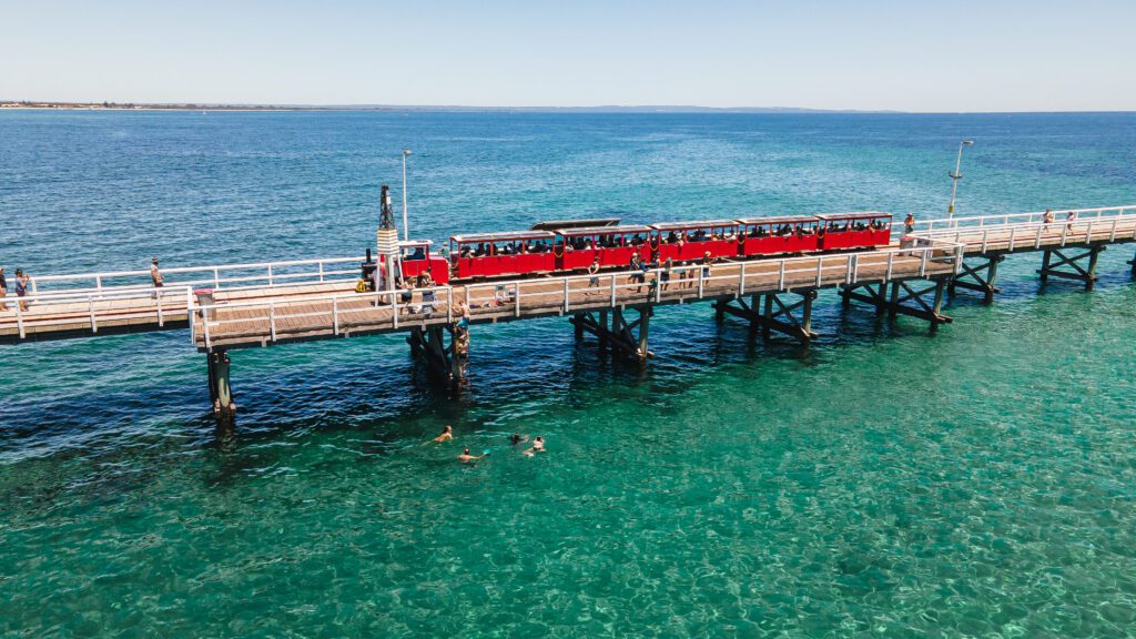 The red Jetty Train travelling back to shore above the blue waters of Geographe Bay.