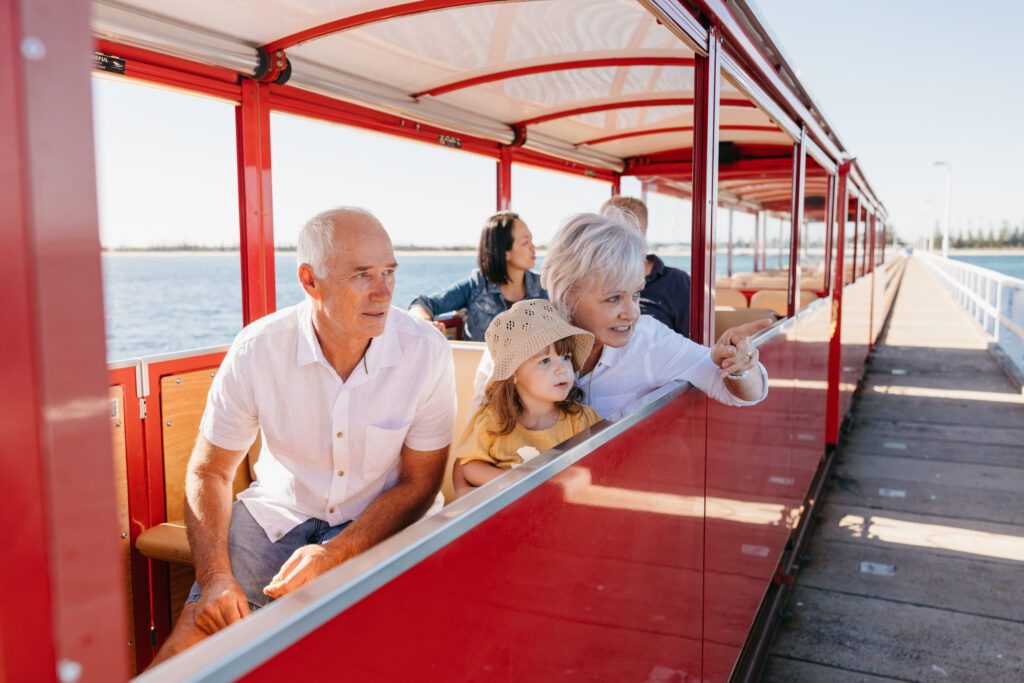 Two grandparents and their granddaughter riding the Busselton Jetty Train while pointing out to the ocean.